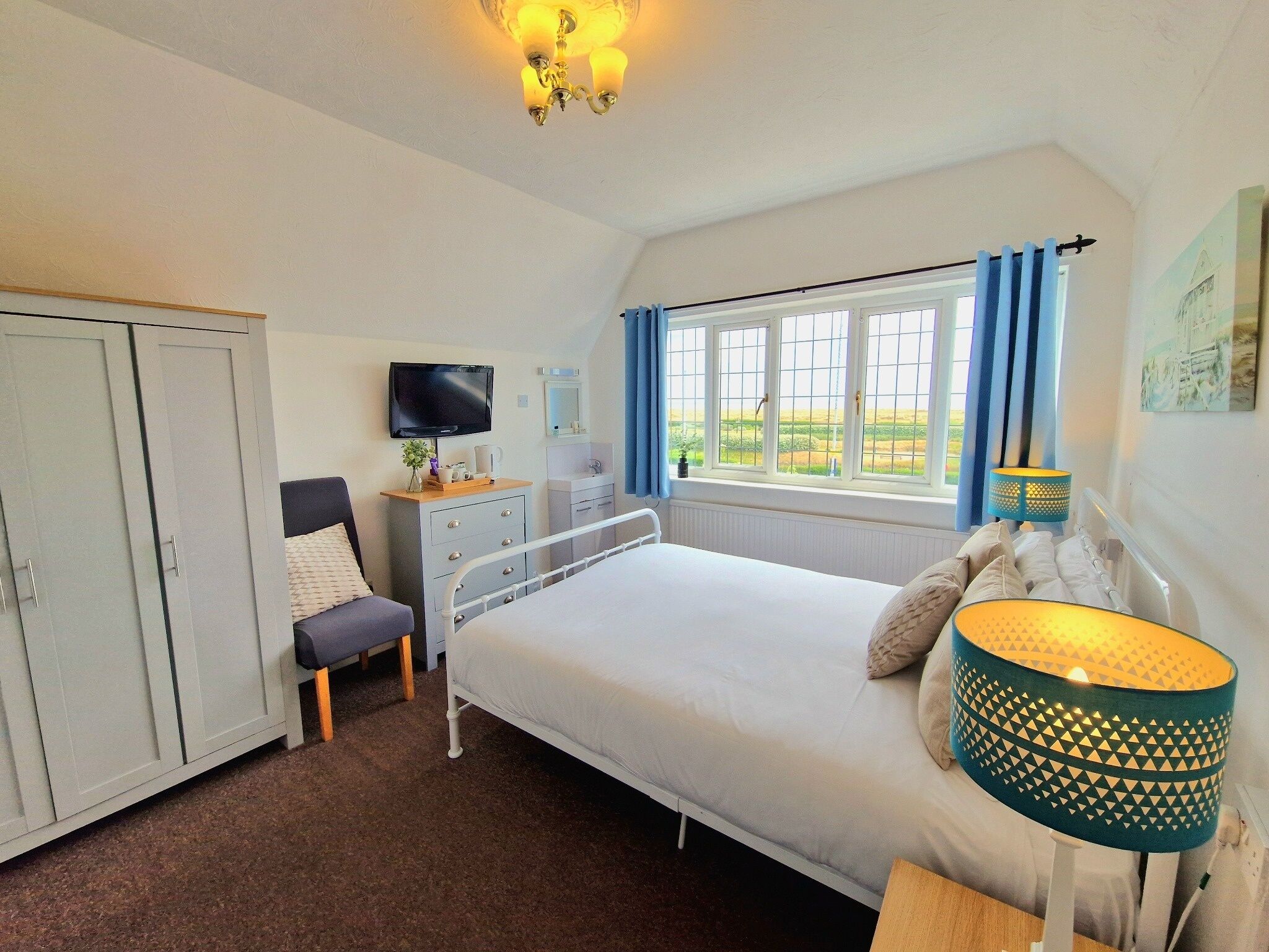 A bedroom with a bed, a desk, a television, a wardrobe, and a window with curtains.