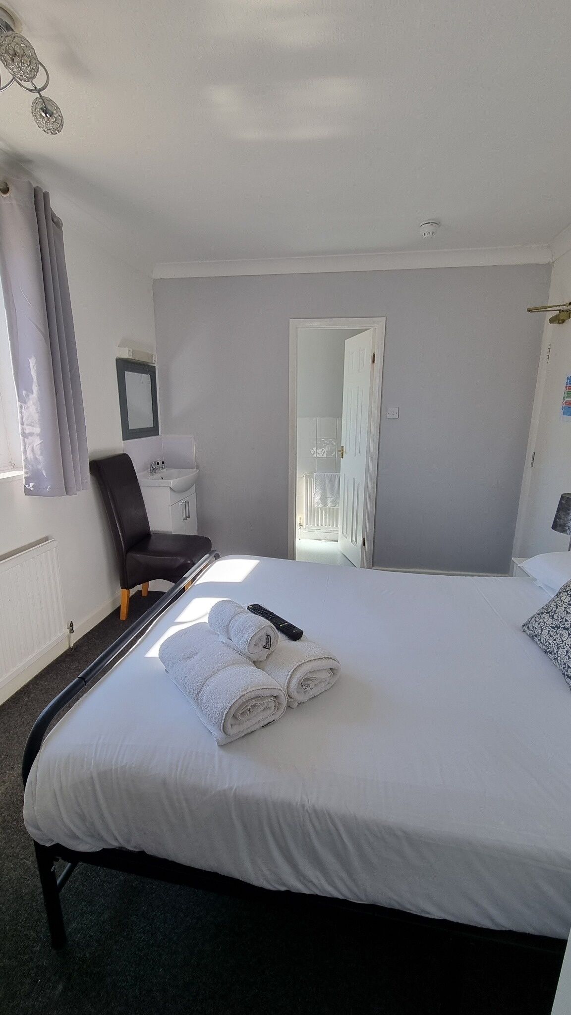 A hotel room with a bed, a chair, a desk with a sink, and a door leading to a bathroom.