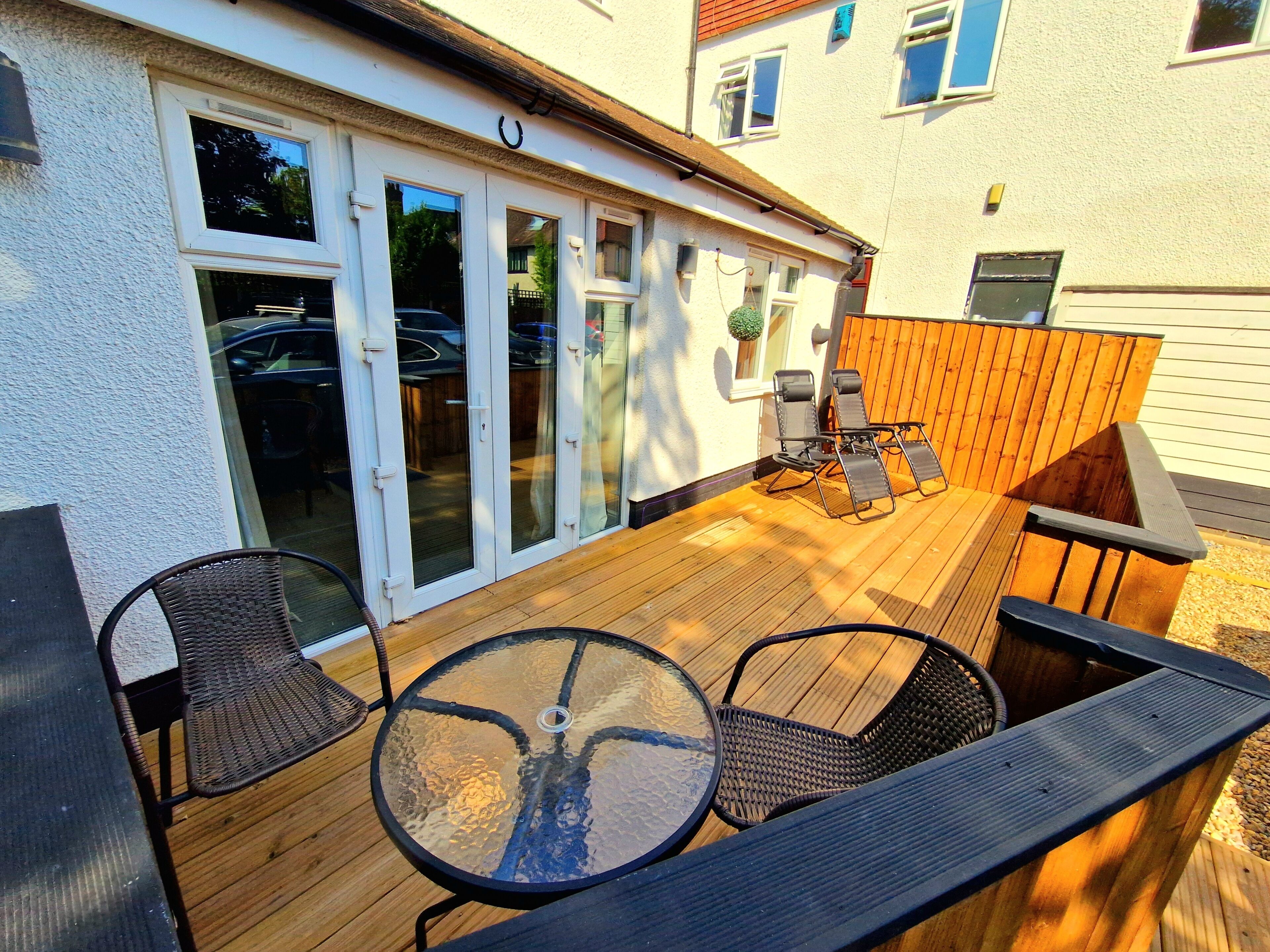 A wooden deck with a glass door entrance, outdoor furniture, and a small garden area.