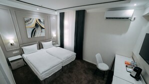 A hotel room with a double bed, a desk with a chair, an air conditioning unit, and a painting on the wall. - Central Plaza (Urgench)