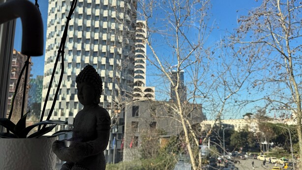 Una estatua de Buda en un alféizar con vista a un edificio alto y árboles desnudos.