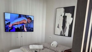 Un dormitorio con una cama, un televisor montado en la pared y un cuadro sobre la cama.