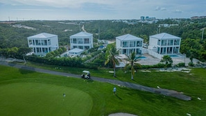 Un campo de golf con tres edificios blancos modernos, cada uno con un balcón grande y una piscina.