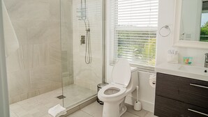 A modern bathroom with a glass-enclosed shower, a toilet, a sink, and a window with blinds.