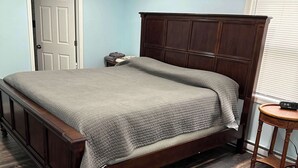 A bedroom with a wooden bed, a nightstand, a door, and a window with blinds.