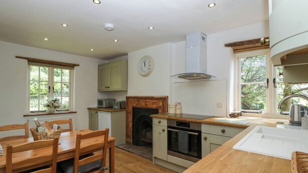 A kitchen with wooden furniture, a fireplace, and a clock on the wall. - Pennfields (Blakeney)