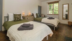 A bedroom with two beds, a window, a mirror, and a bedside table with lamps. - Pennfields (Blakeney)