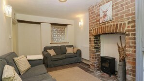A cozy living room with a brick fireplace, a grey sofa, and a patterned rug. - Pennfields (Blakeney)