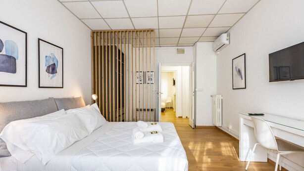 Et moderne hotelværelse med seng, skrivebord, stol og billeder på væggene.