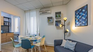 En moderne stue med en grå sofa, et spisebord med stole, et køkkenområde og en vægmonteret aircondition.