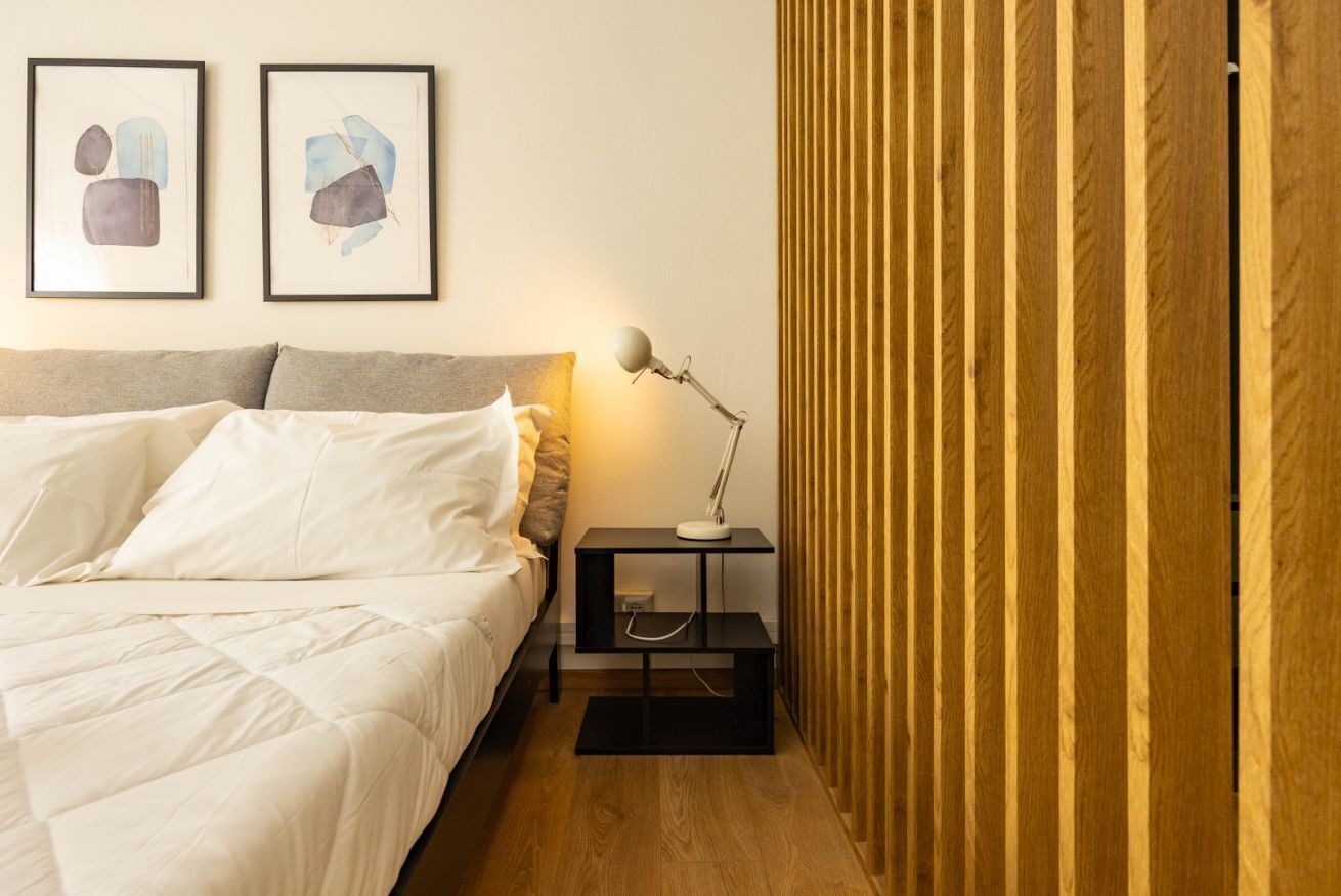 A bedroom with a bed, bedside table with a lamp, and two framed abstract paintings on the wall.