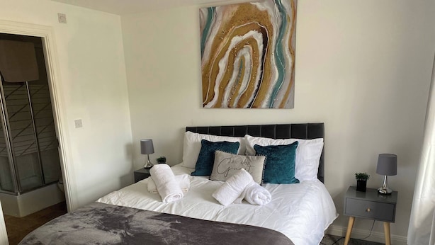 A neatly made bed with white linens and a gray throw blanket, a headboard with teal pillows, and a modern abstract painting above.