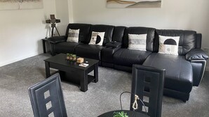 A modern living room with a black leather sofa, a coffee table, and two chairs. There are two wall-mounted artworks and a floor lamp.