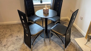 A small dining area with a round table and four black chairs, a tissue box on the table, and a window with a view of a garden.