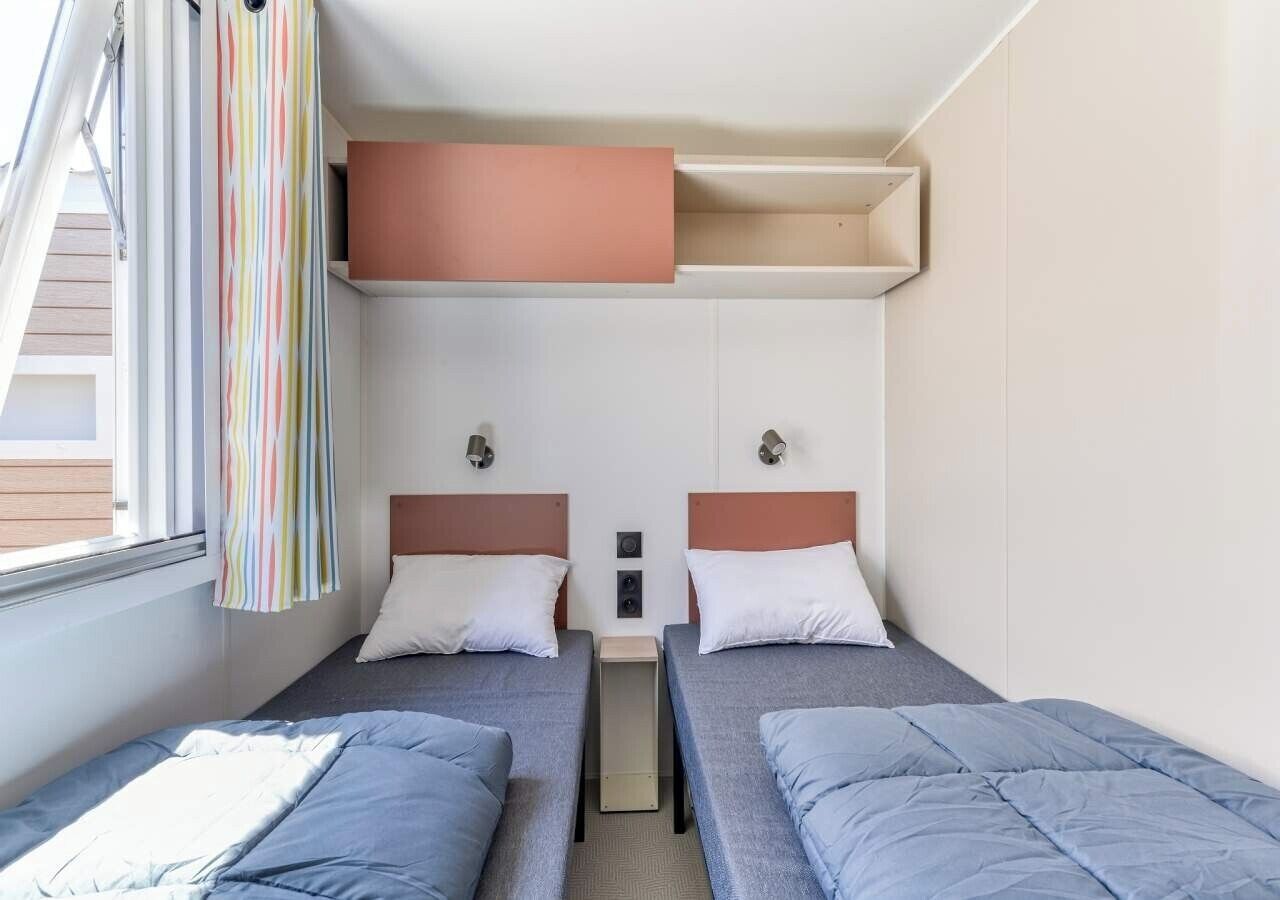 A hotel room with two beds, a window with curtains, and a small table between the beds.