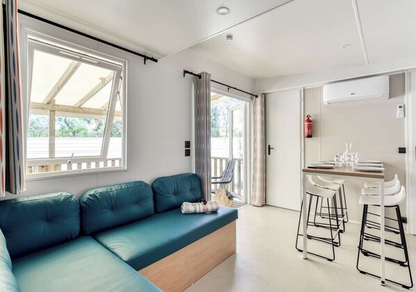 A modern room with a blue sofa, a small table with chairs, and a sliding door leading to an outdoor area. - Camping Park Umag - Eurocamp (Brtonigla)