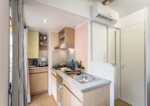 Una cocina compacta con estufa integrada, un lavamanos y una pequeña encimera. Hay un armario con vajilla y una cafetera.