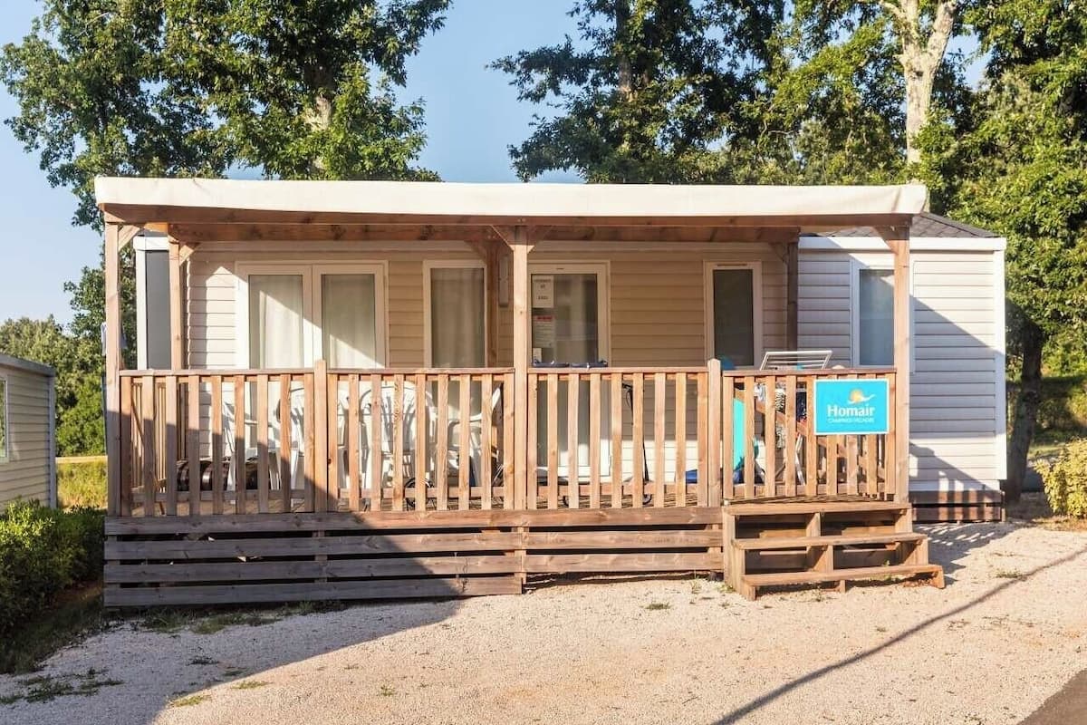 A small, single-story cabin with a wooden deck and a covered porch.