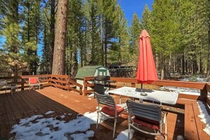 Eine Holzdielen-Terrasse mit Tisch und Stühlen, umgeben von hohen Kiefern.
