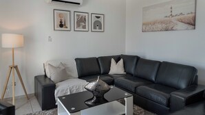 A modern living room with a black leather sofa, a glass coffee table, and a lamp. There are three framed artworks on the wall. - Phaedrus Living: Seaview Hilltop Maisonette (Chlorakas)