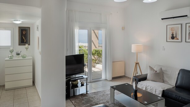 A modern living room with a TV, sofa, coffee table, and a view of the outdoors. - Phaedrus Living: Seaview Hilltop Maisonette (Chlorakas)