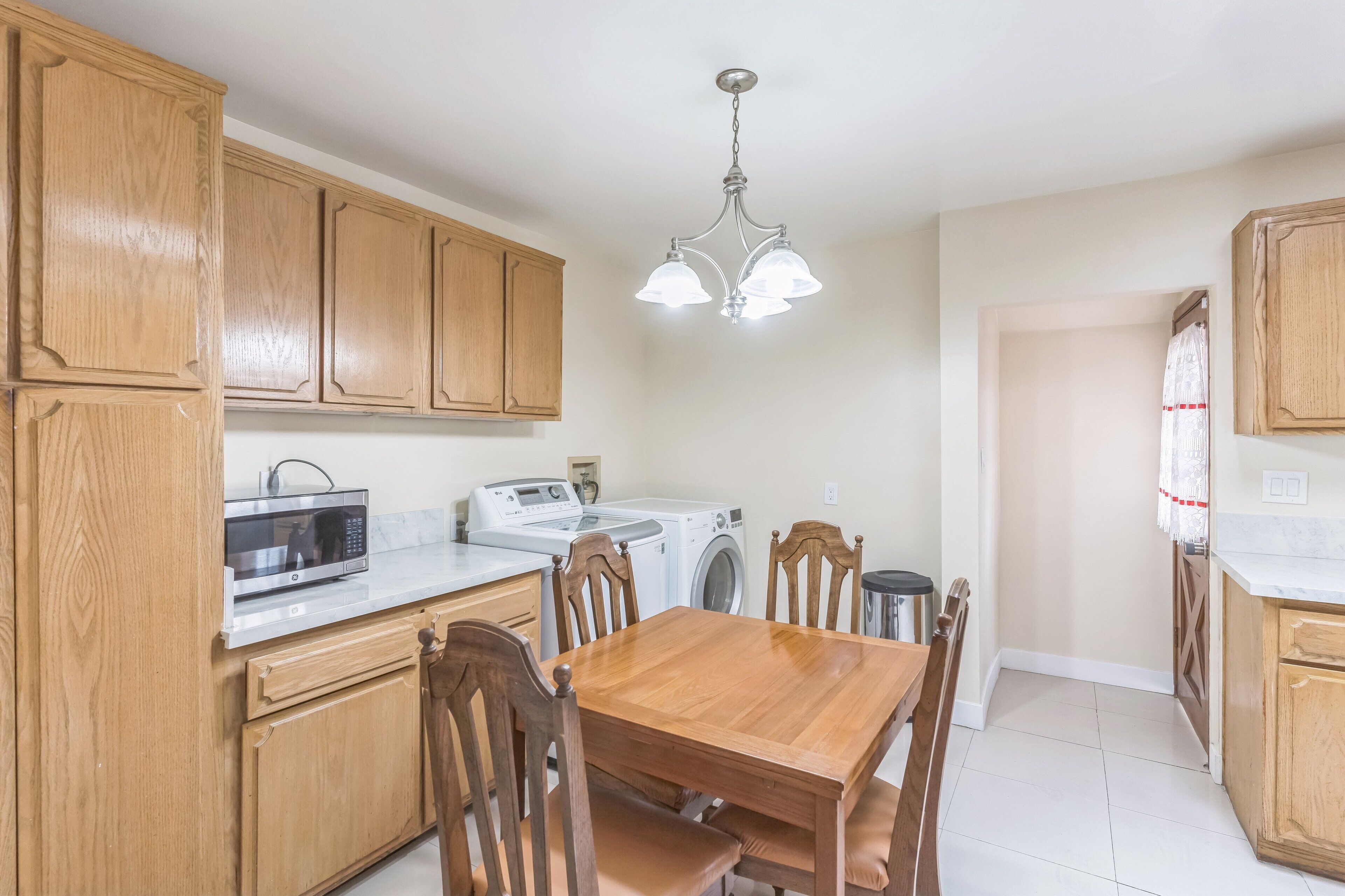 A kitchen with wooden cabinets, a microwave, a washing machine, and a dining table with chairs.