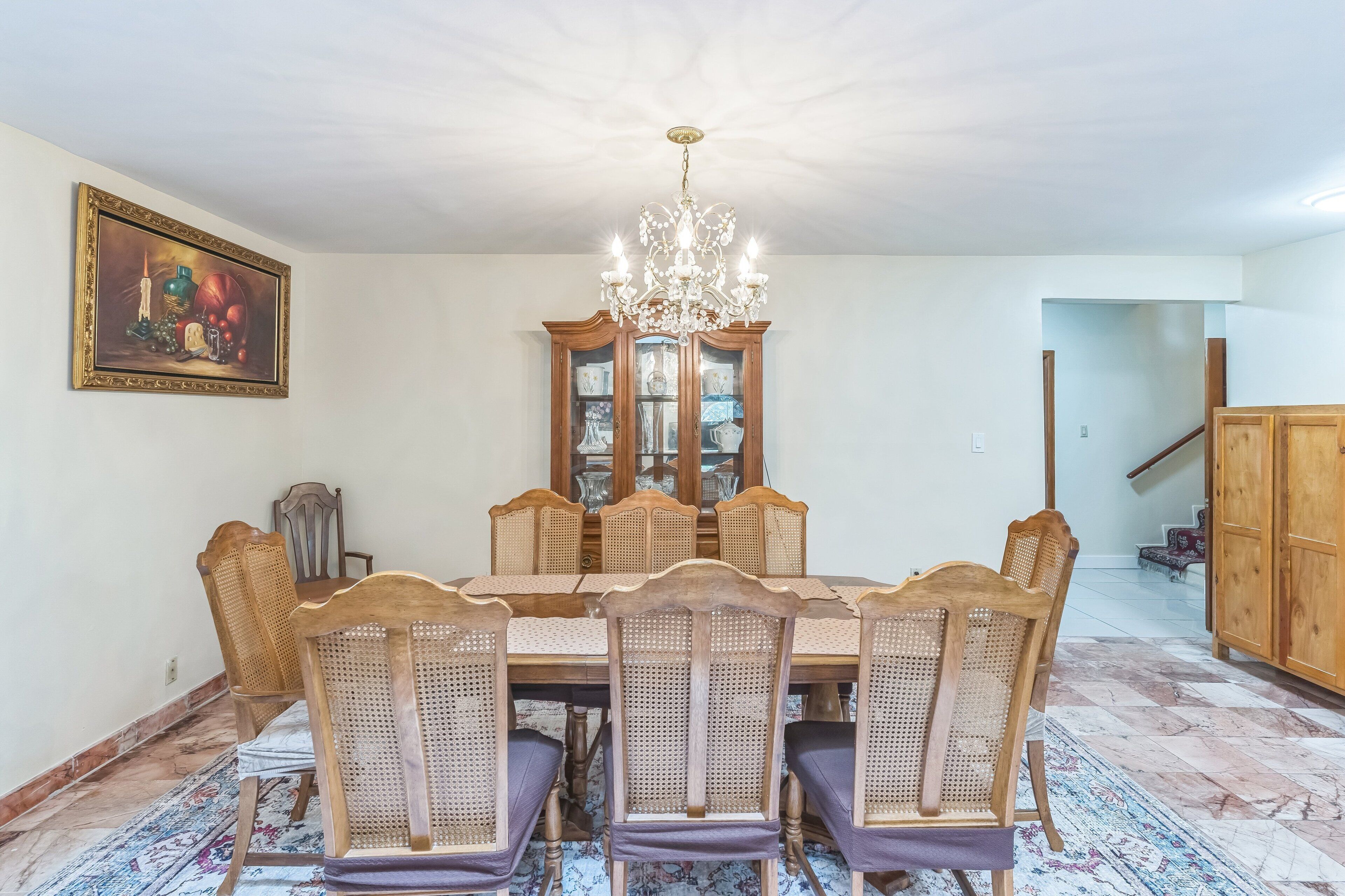 A dining room with a wooden table, six chairs, a chandelier, and a cabinet with glass doors.