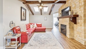 A living room with a red leather sofa, a patterned rug, a stone fireplace, and a ceiling fan. - Peaceful Horse Ranch Escape Near Palo Duro Canyon 3 Bedroom Home (Canyon)