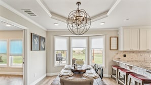A dining area with a wooden table set for four, a chandelier, and a view of the outdoors through large windows. - Peaceful Horse Ranch Escape Near Palo Duro Canyon 3 Bedroom Home (Canyon)