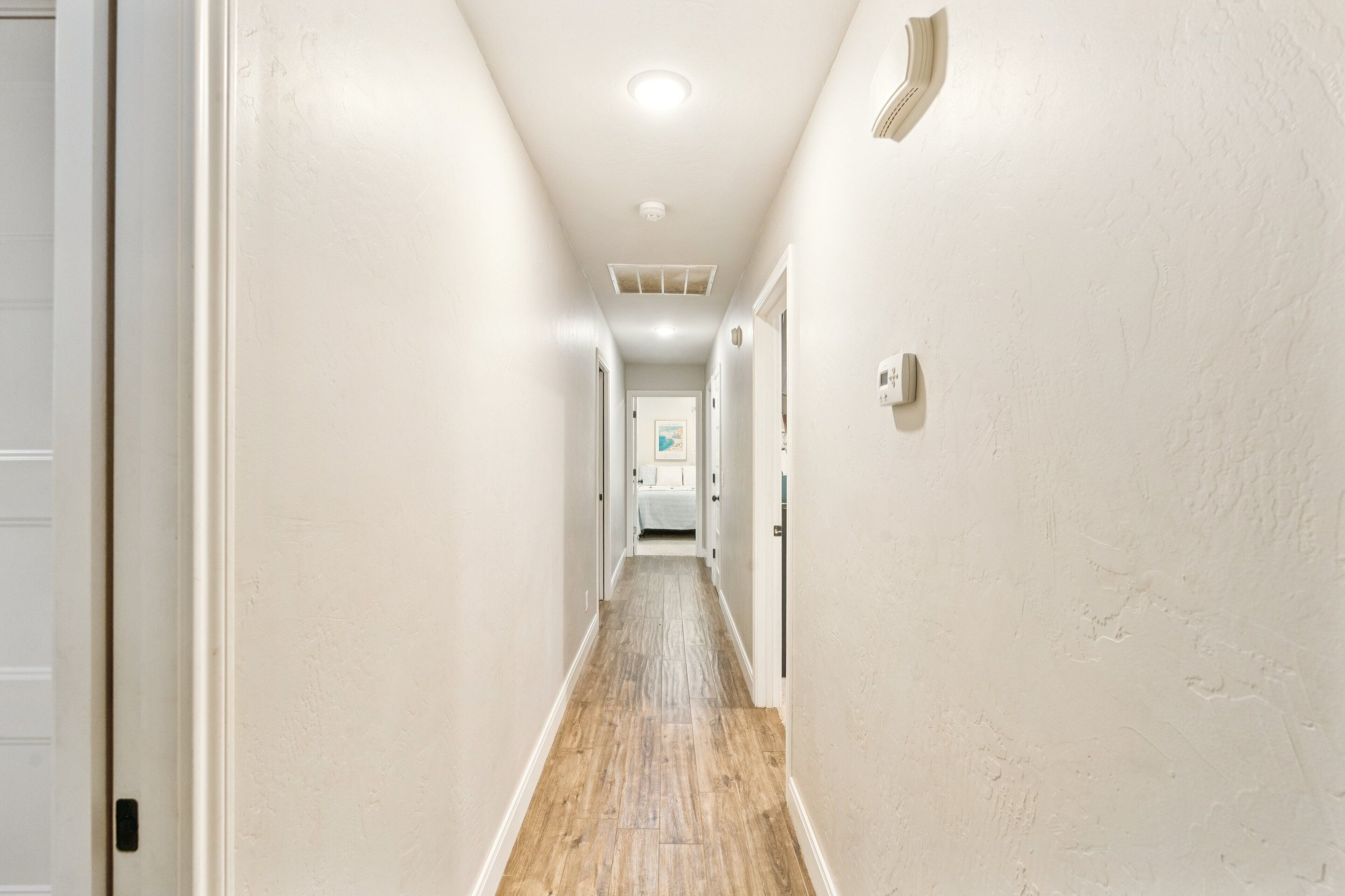 A narrow, well-lit hallway with wooden flooring and white walls.