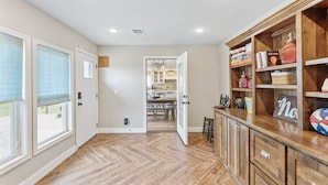 A spacious hallway with wooden flooring, a kitchen visible through an open door, and a wooden bookshelf with various items. - Peaceful Horse Ranch Escape Near Palo Duro Canyon 3 Bedroom Home (Canyon)