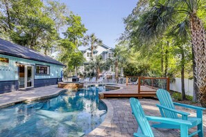 A swimming pool with a stone edge, surrounded by a wooden deck and a few chairs. - Sunset Rentals | Heron 7 | Dog Friendly (Hilton Head Island)