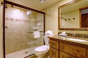 A bathroom with a glass-enclosed shower, a toilet, a sink with a mirror above it, and wooden cabinets. - Wl210 West Lake Lodge 2 Bedroom Condo (Copper Mountain)