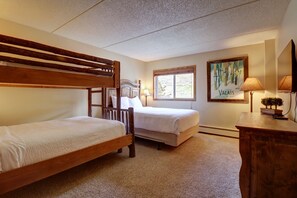 A bedroom with two wooden bunk beds, a single bed, a desk with a lamp, a window with a view, and a painting on the wall. - Wl210 West Lake Lodge 2 Bedroom Condo (Copper Mountain)