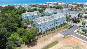 A coastal residential area with light blue buildings, a clear view of the ocean, and a well-maintained lawn. - Rooftop Terrace | Garage | Near Beach (Santa Rosa Beach)