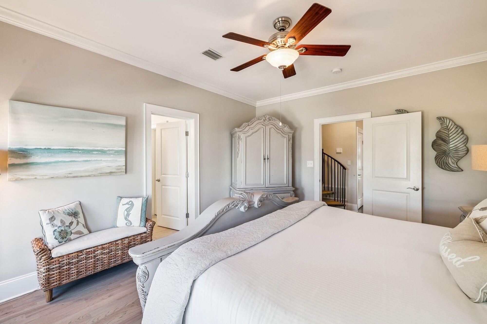 A bedroom with a large bed, a ceiling fan, a wardrobe, and a painting on the wall.