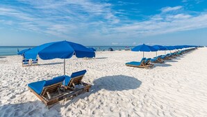 Een strand met rijen blauwe parasols en houten ligstoelen.