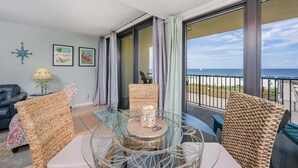 Een balkon met rieten stoelen, een glazen tafel en uitzicht op de oceaan.