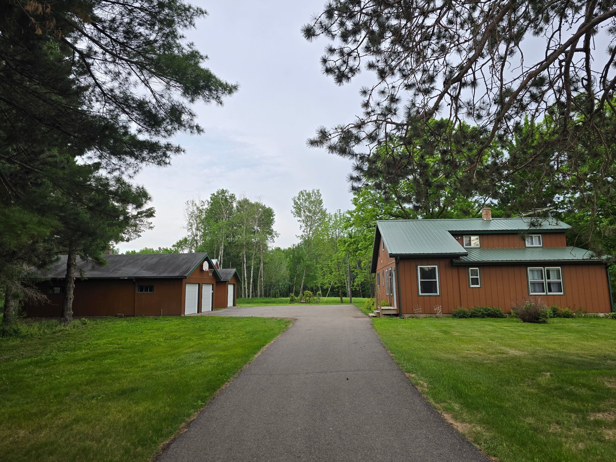A two-story wooden cabin with a green roof, surrounded by a well-maintained lawn and tall trees.