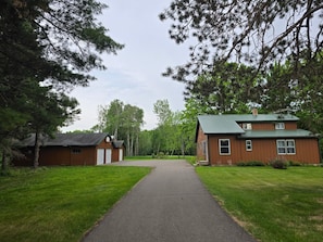 A two-story wooden cabin with a green roof, surrounded by a well-maintained lawn and tall trees.