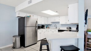 A modern kitchen with white cabinets, stainless steel appliances, a central island, and a trash can. - Beachfront 1BR, Updated with great amenities! (Orange Beach)