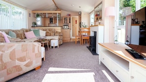 A compact living space with a sofa, a small table, a kitchen area, and a fireplace. - 152 Central Park (Prestatyn)
