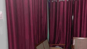 Une pièce comprenant deux chaises en bois à assise tressée, un petit tabouret et un rideau servant de séparation.