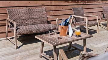 Des meubles en osier, une table en bois et un récipient contenant des bouteilles et des verres, le tout posé sur une terrasse en bois.