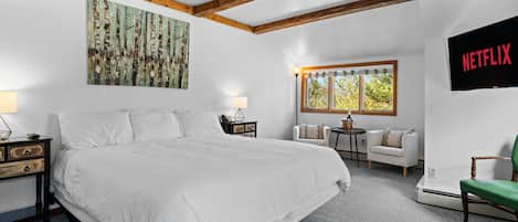 A bedroom with a large bed, a TV mounted on the wall, a window with a view, and a painting on the wall.