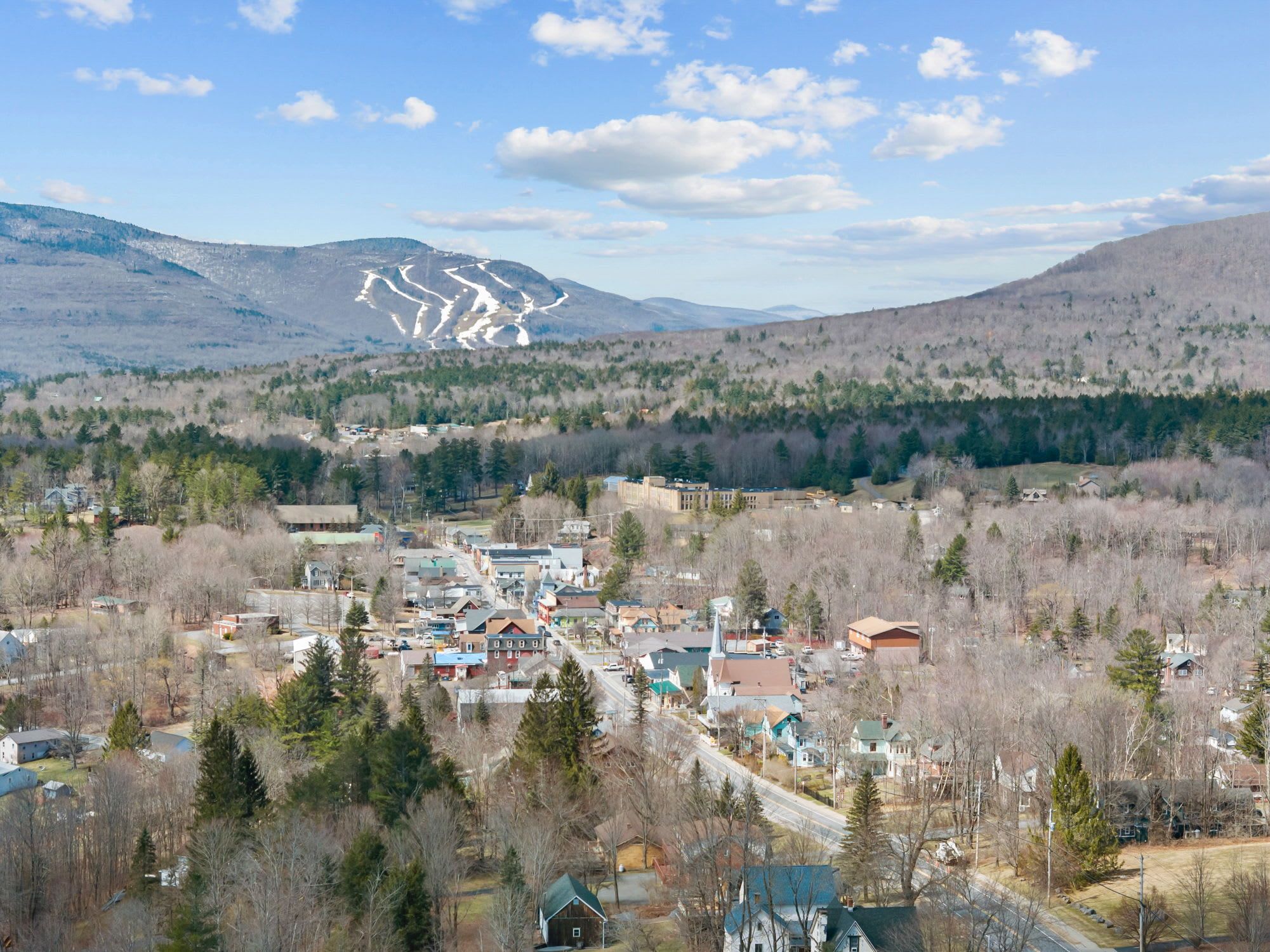 A town with a central road, buildings, and a mountain with snow patches in the background.