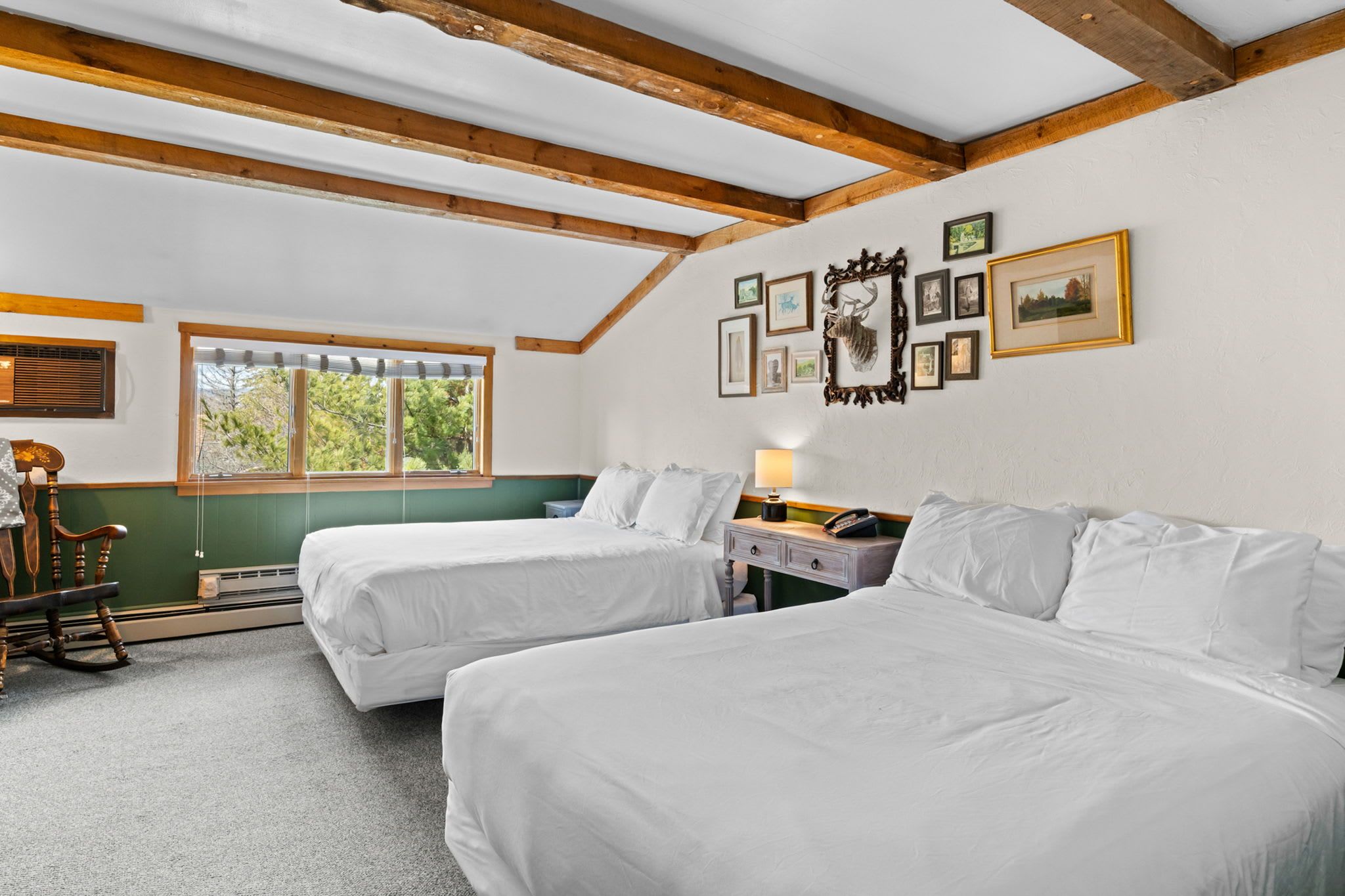 Quarto com duas camas, uma cadeira de balanço, escrivaninha com luminária e janela com persianas.