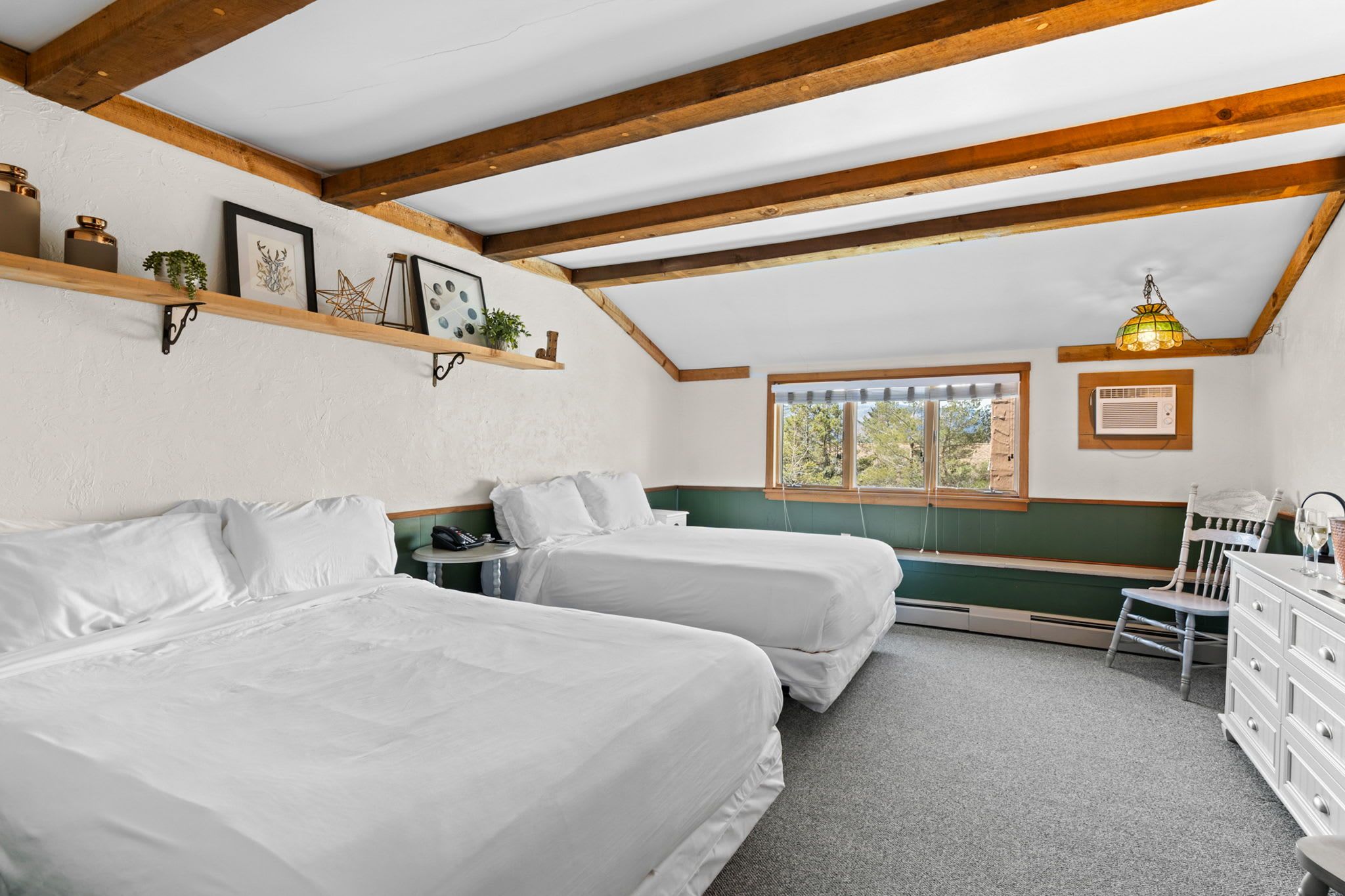 Une chambre avec deux lits, des poutres en bois, une fenêtre donnant sur un beau paysage, un bureau et une chaise.