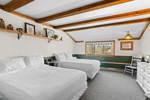 A bedroom with two beds, wooden beams, a window with a view, a desk, and a chair.
