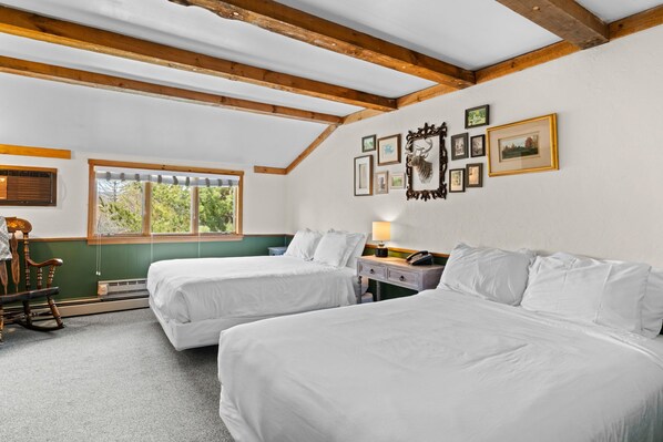A room with two beds, a rocking chair, a desk with a lamp, and a window with blinds.